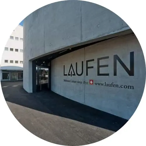 Laufen company sign on concrete wall outside modern building entrance with Swiss flag and website URL