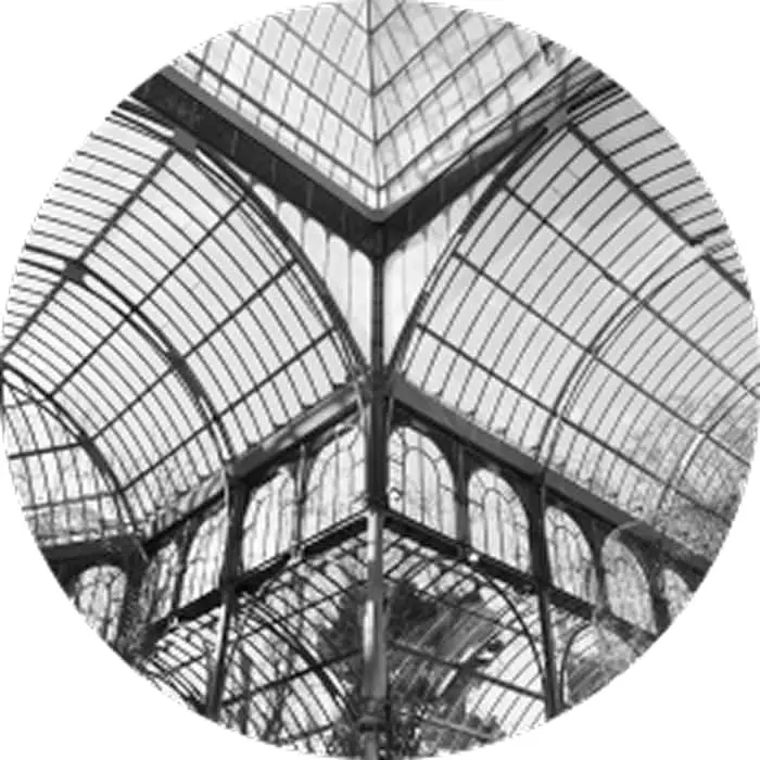 Black and white photo of a glass and metal structure with arched roof and geometric patterns viewed from below.