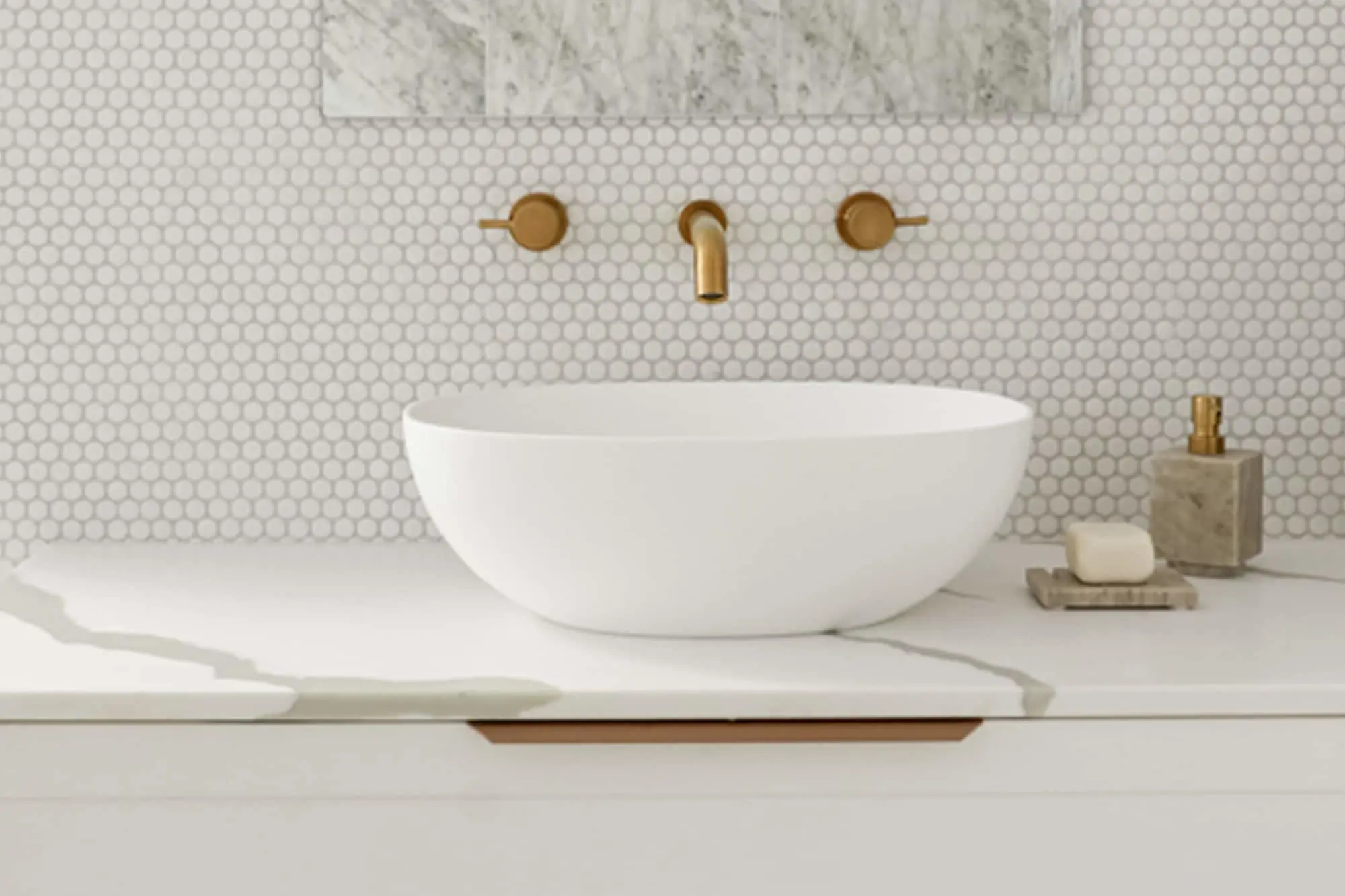 White bowl sink on marble counter with brass wall-mounted faucet and white penny tile backsplash