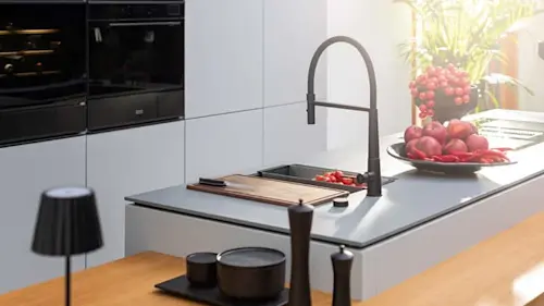 Modern kitchen with white cabinets, gray countertop, black faucet, and fresh red fruit on display.