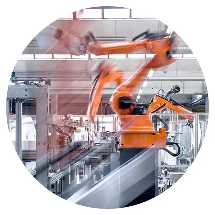 Orange robotic arms in motion on a factory assembly line inside an industrial facility.