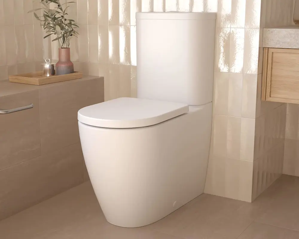 White modern toilet in a beige tiled bathroom with natural light from window and decorative vase on counter.