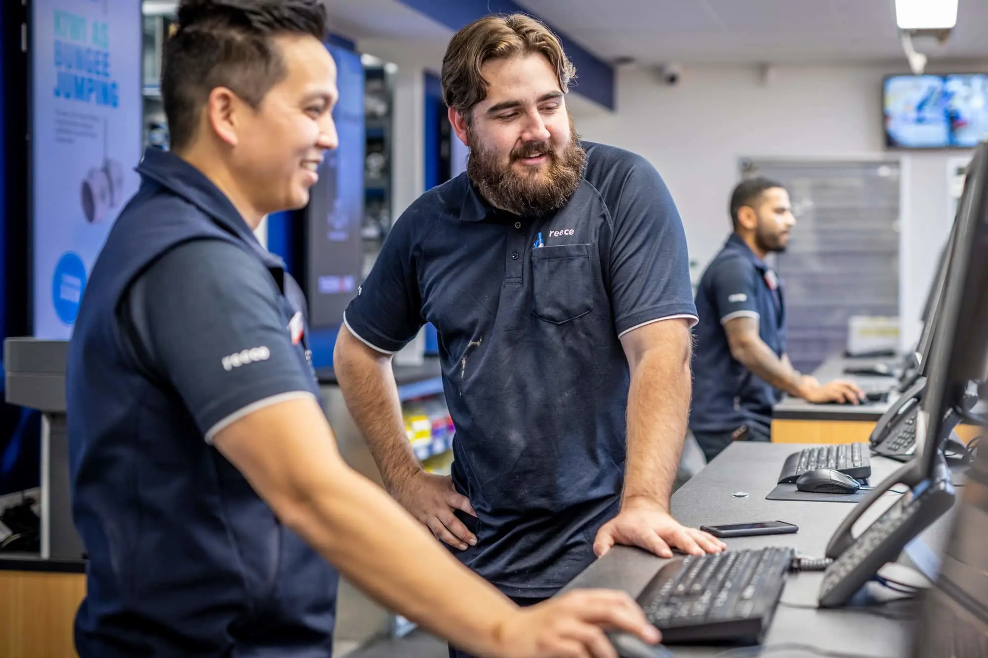 Three employees in dark polo shirts working at computer workstations in an office environment.