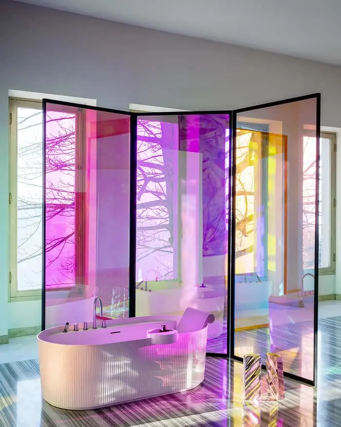 Modern bathroom with freestanding tub and colorful glass panels casting pink, purple, and yellow light reflections.