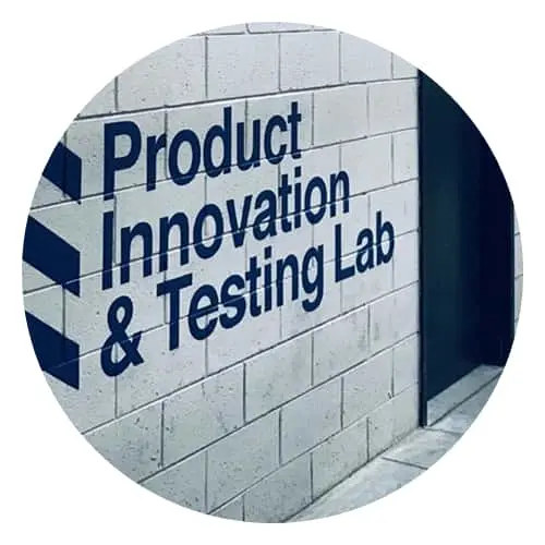 Blue text reading Product Innovation & Testing Lab painted on white brick wall with diagonal striped border