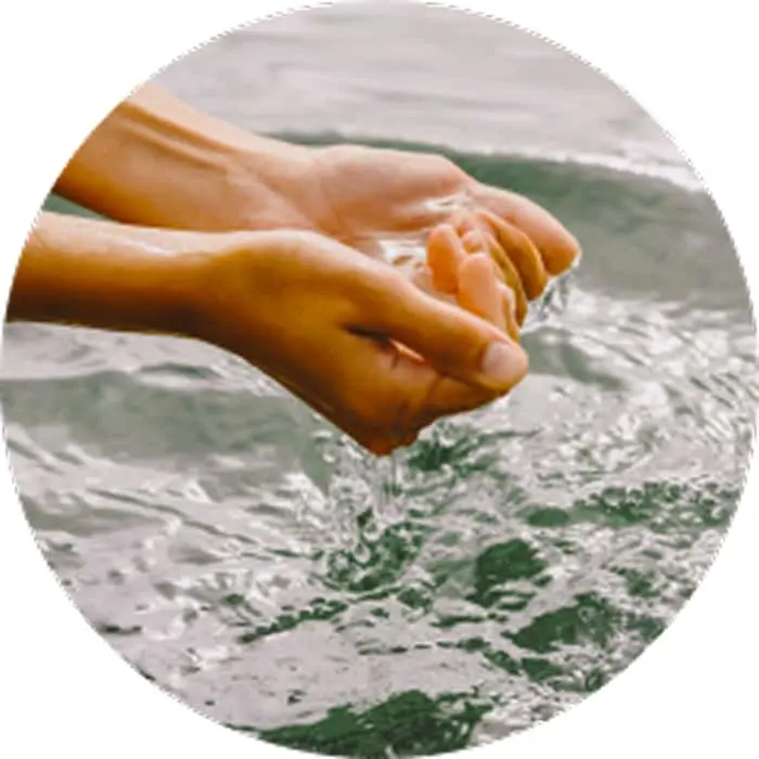 Hands cupped together holding water with splashing droplets in a circular frame