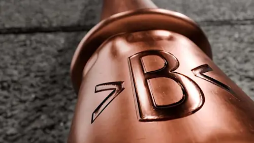 Close-up of a copper-colored pipe with embossed letters and numbers on its surface against a gray background.
