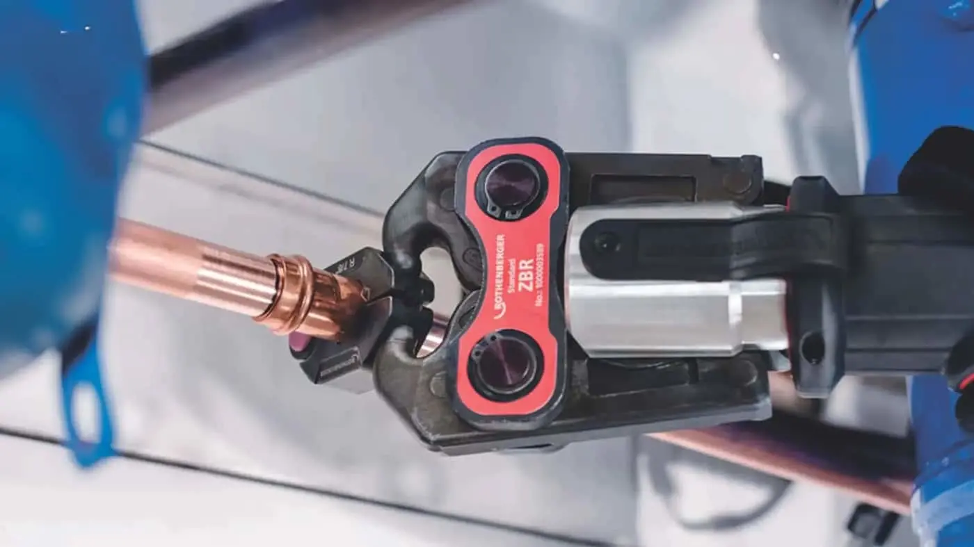 Pipe cutting tool with red and black housing gripping a copper pipe on a workbench.