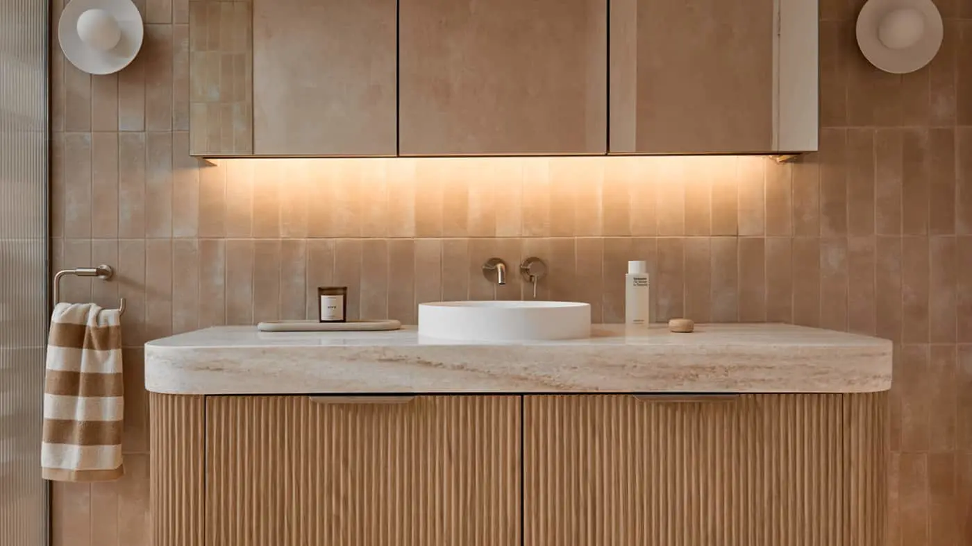 Bathroom vanity with white vessel sink on marble countertop, beige tile walls, under-cabinet lighting, and striped towel.