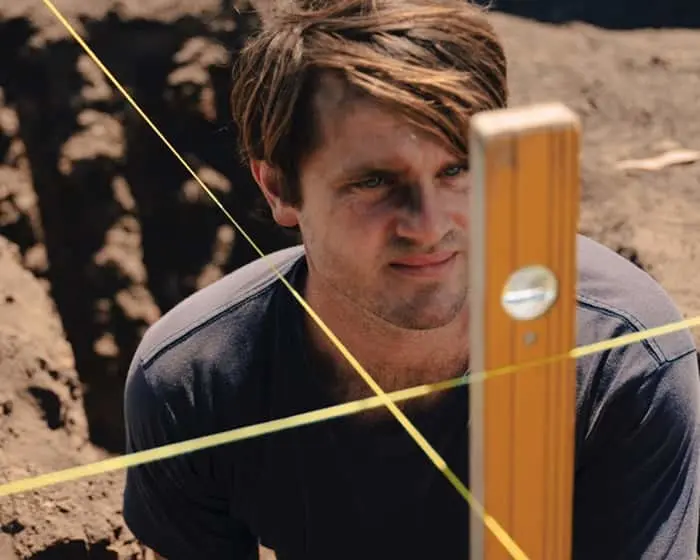 Man looking at camera with yellow string and wooden level in foreground on construction site
