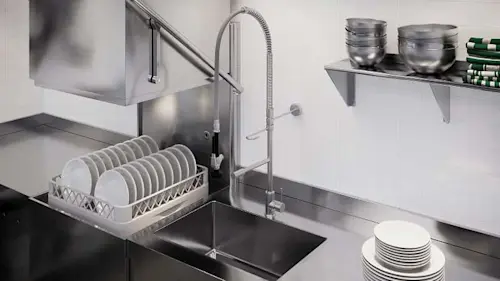 Commercial kitchen with stainless steel sink, dish rack with white plates, and wall-mounted shelf with bowls.