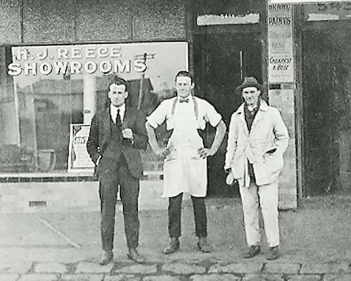 Three men standing in front of H.J. Showrooms storefront in vintage black and white photograph