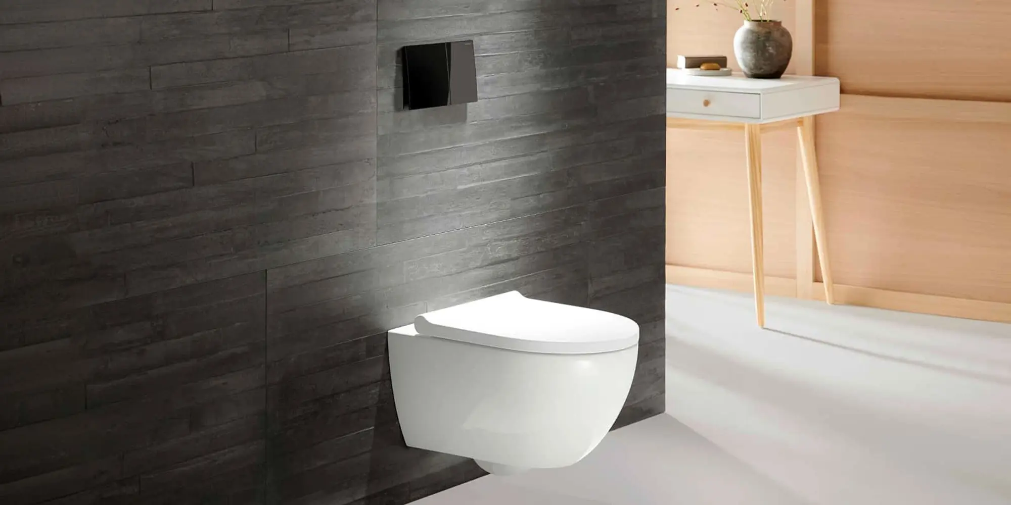 White wall-mounted toilet against dark gray wood-textured tile wall with black flush plate and side table visible.