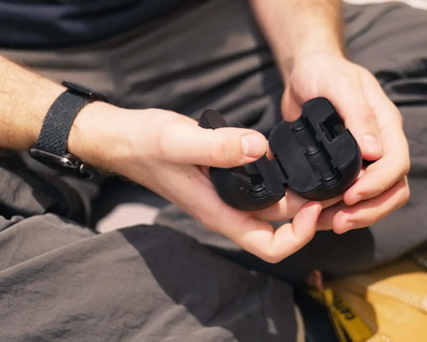 Hands holding two black plastic clips or connectors against a gray fabric background.