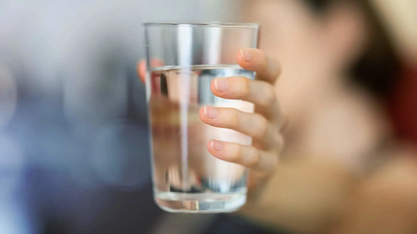 Person holding a clear glass of water with blurred background