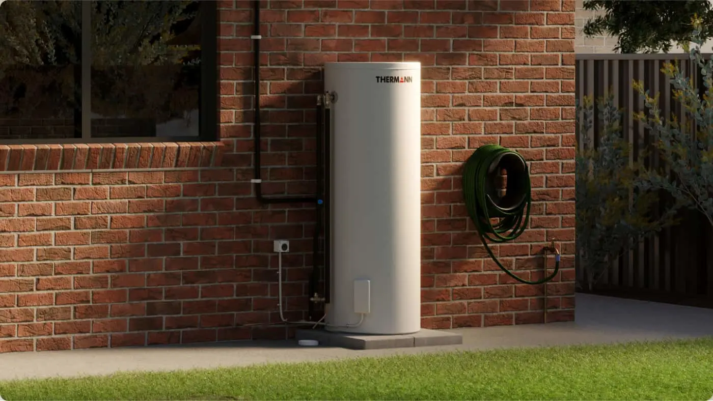 White cylindrical Thermann water heater installed against a red brick wall with a coiled green hose mounted nearby.