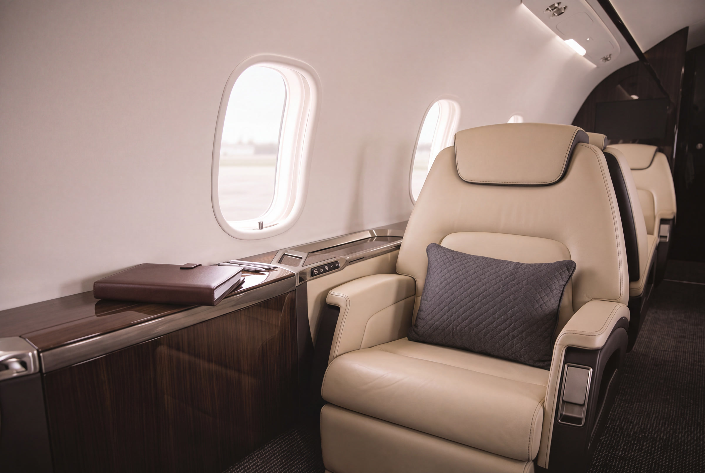 Cream leather business jet cabin seat beside an unmarked records binder.