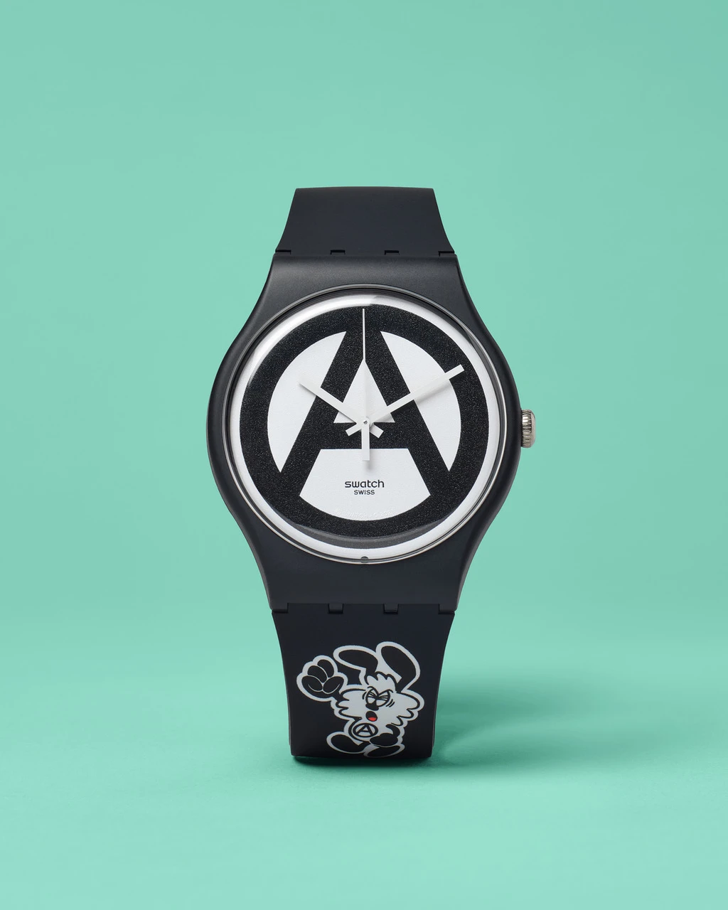 A swatch watch with a black band and a circular face featuring a peace sign design, set against a soft green background. the watch also has a cartoon mouse image near the band's bottom.