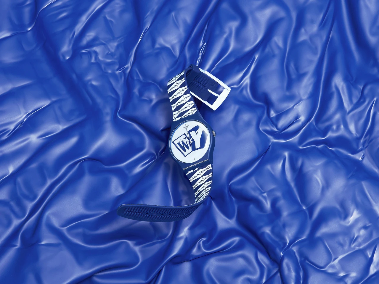 A blue resistance band with white zebra stripes and a white logo on a crinkled blue gym mat background.
