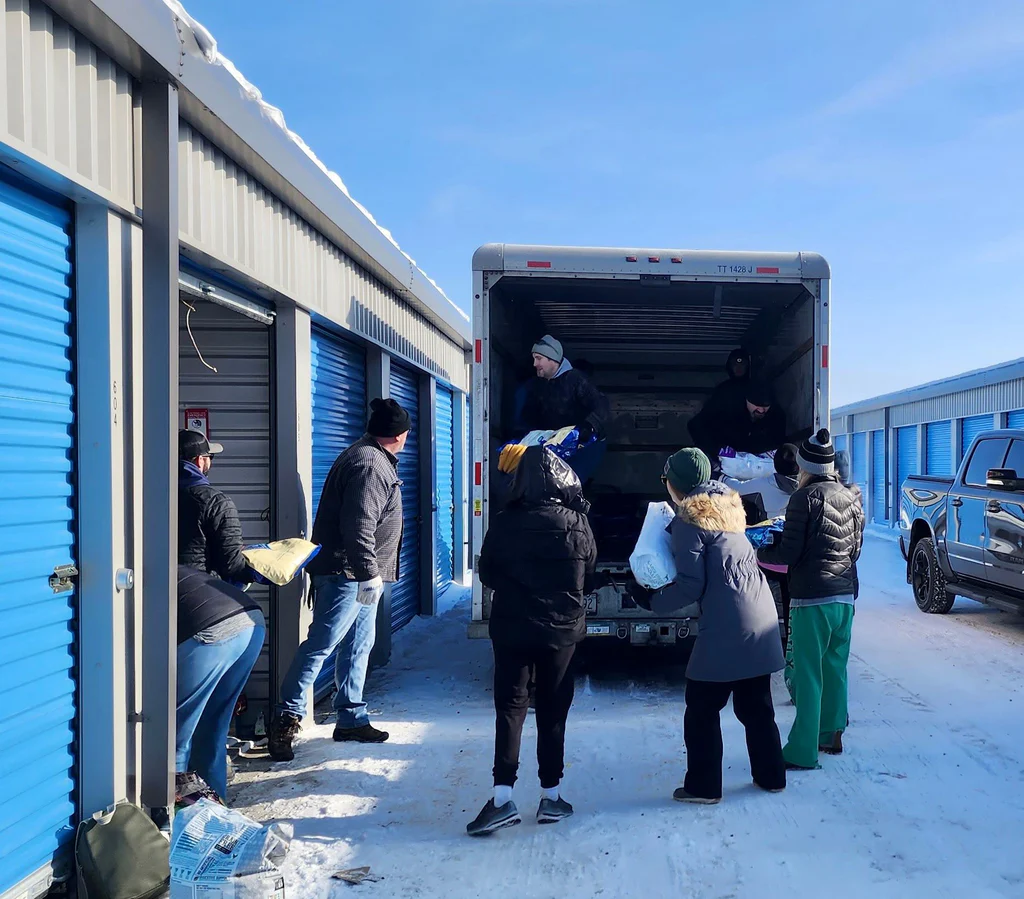 A group of people unloading a large truck of cat supplies together in the winter. 