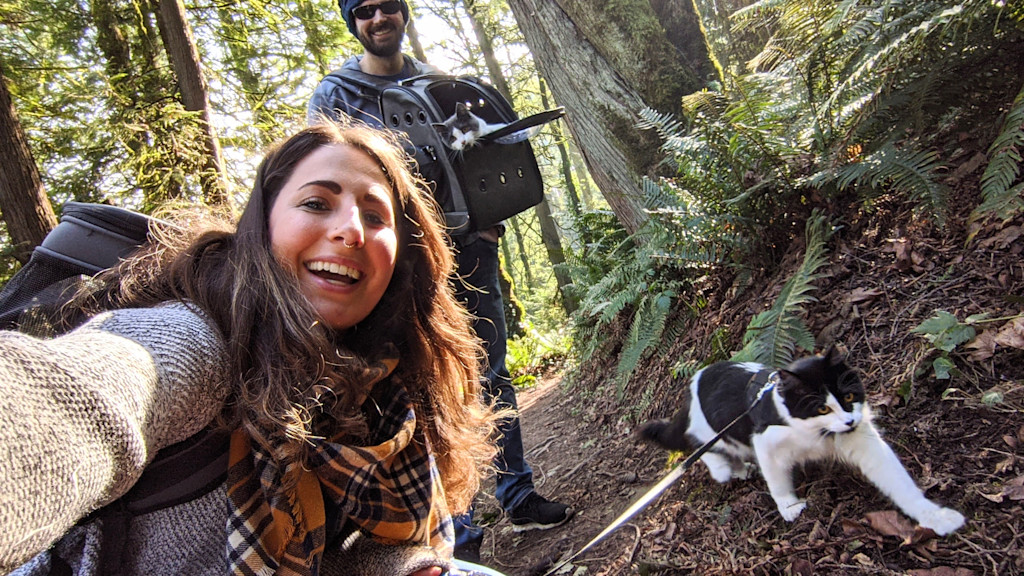 Janelle, her husband, Lyra, and Atlas smile for a selfie while all on a nature hike together.