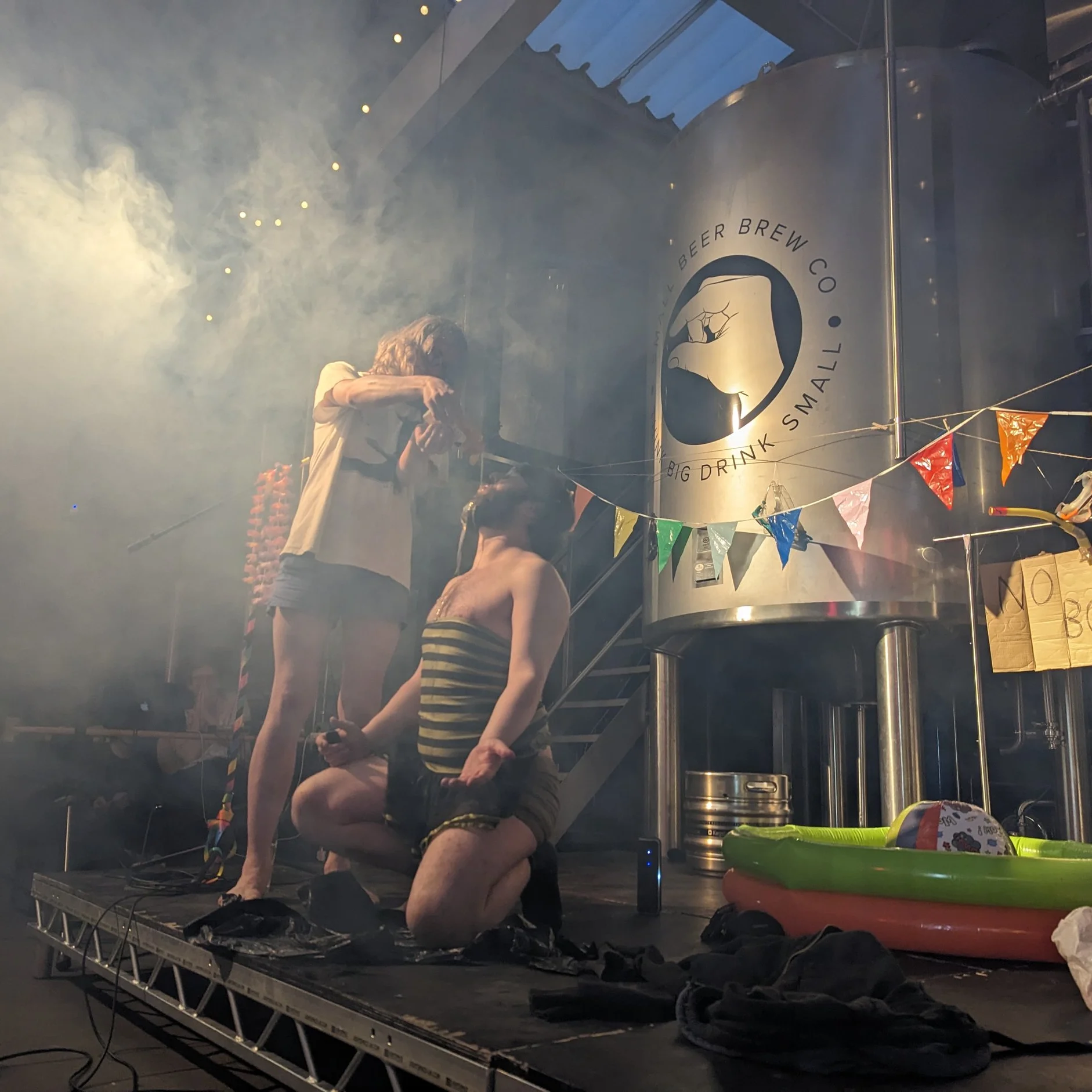 Modern Art Cam & Stephen Cam and Stephen on stage at Modern Art comedy gig. Cam is pouring honey over Stephen, who is dressed like a bumble bee. There's a bunch of smoke in the background and the stage is dressed to look like a summer party.