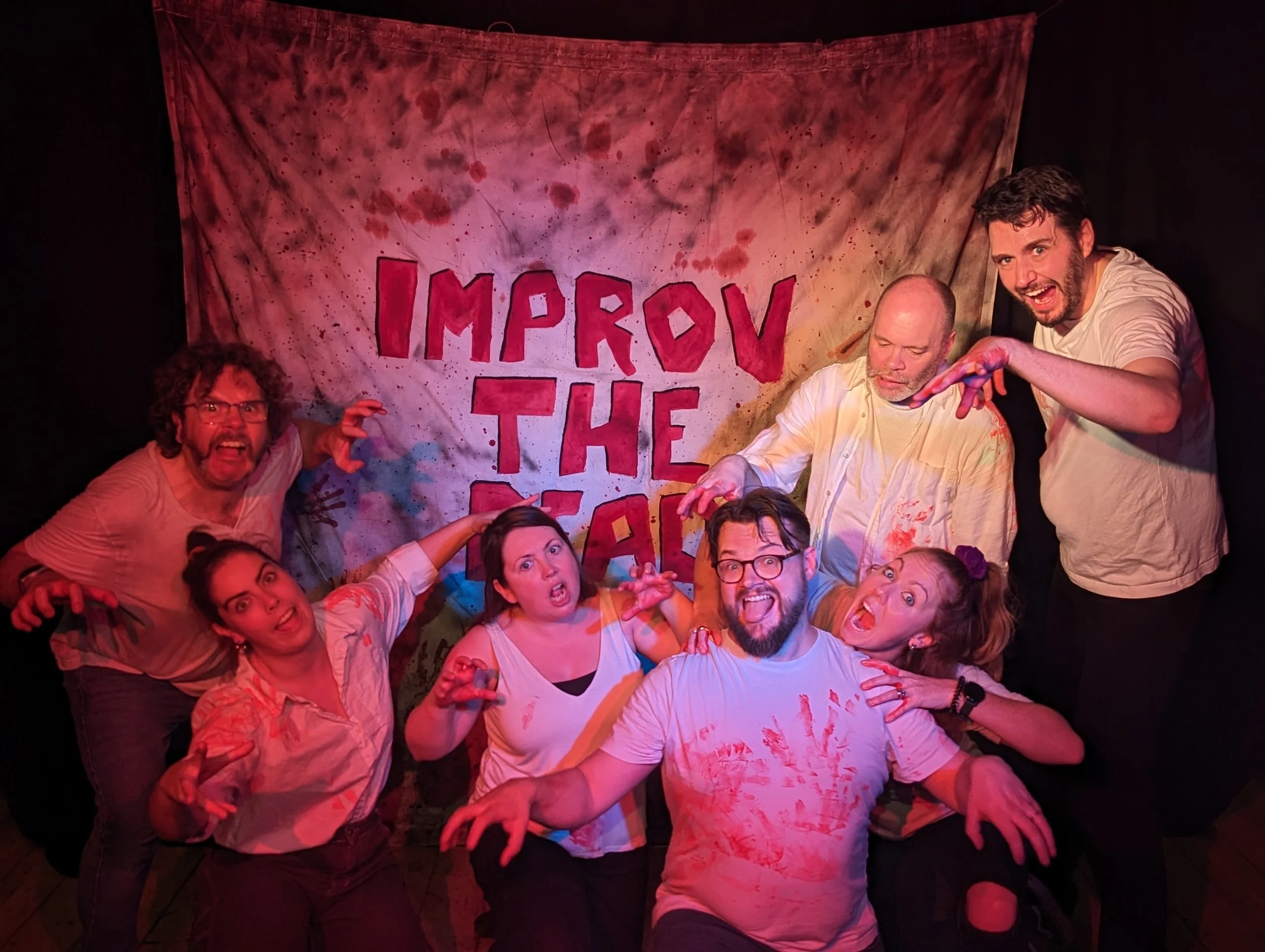 Improv the dead team (6 people) posing like zombies beside their blood stained banner saying Improv The Dead