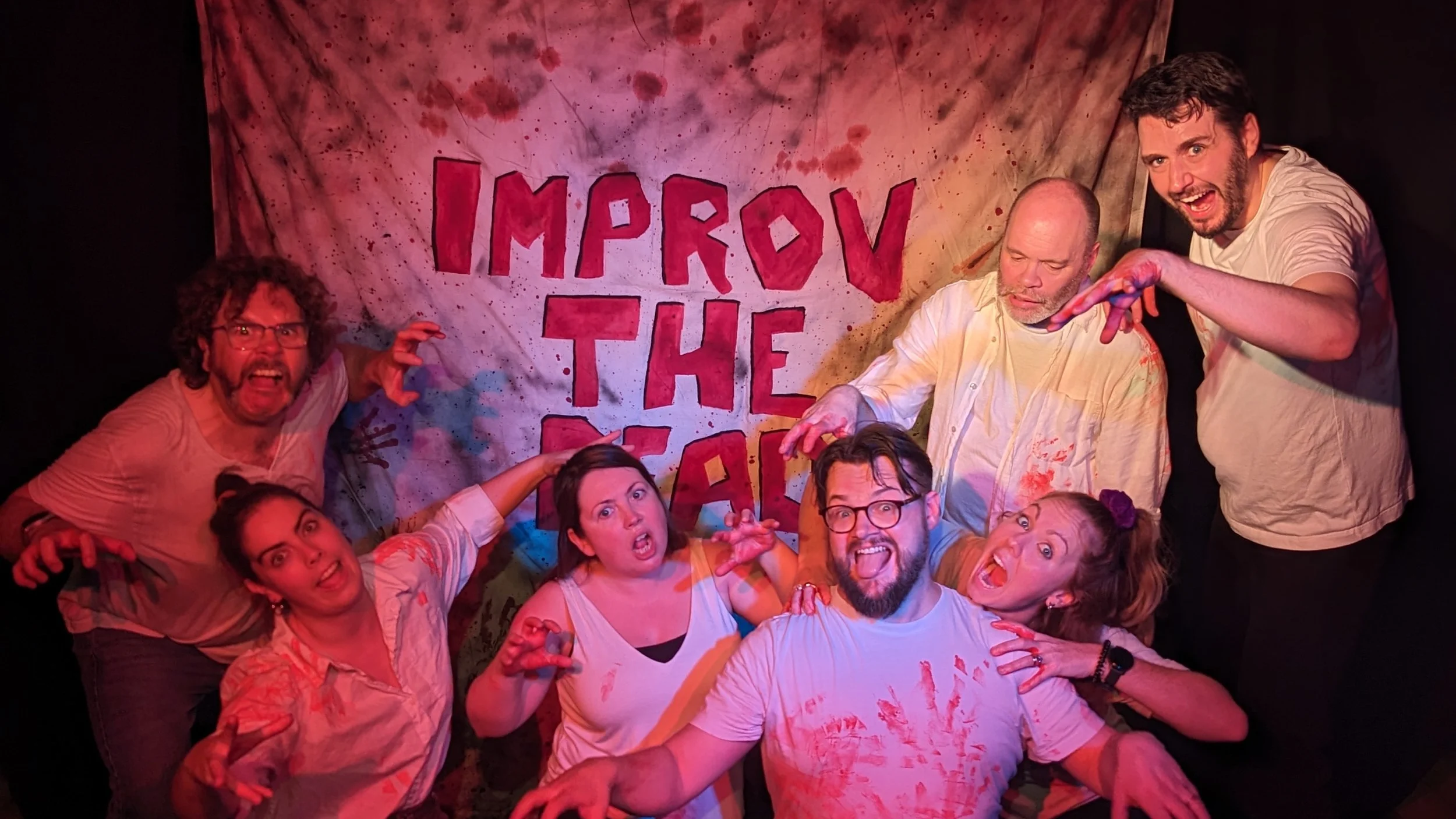 Improv The Dead Brighton Improv the dead team (6 people) posing like zombies beside their blood stained banner saying Improv The Dead