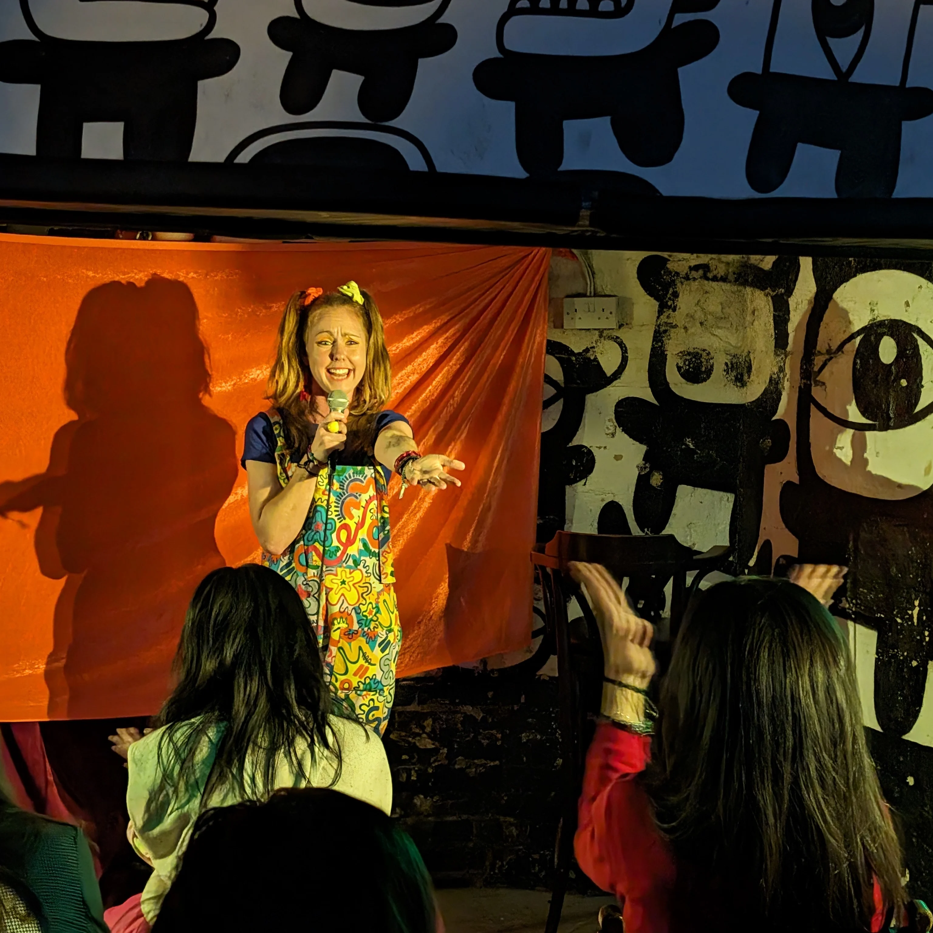 Viki Jackson MA Feb Comedian, Viki Jackson, on stage holding a microphone reaching out to the audience