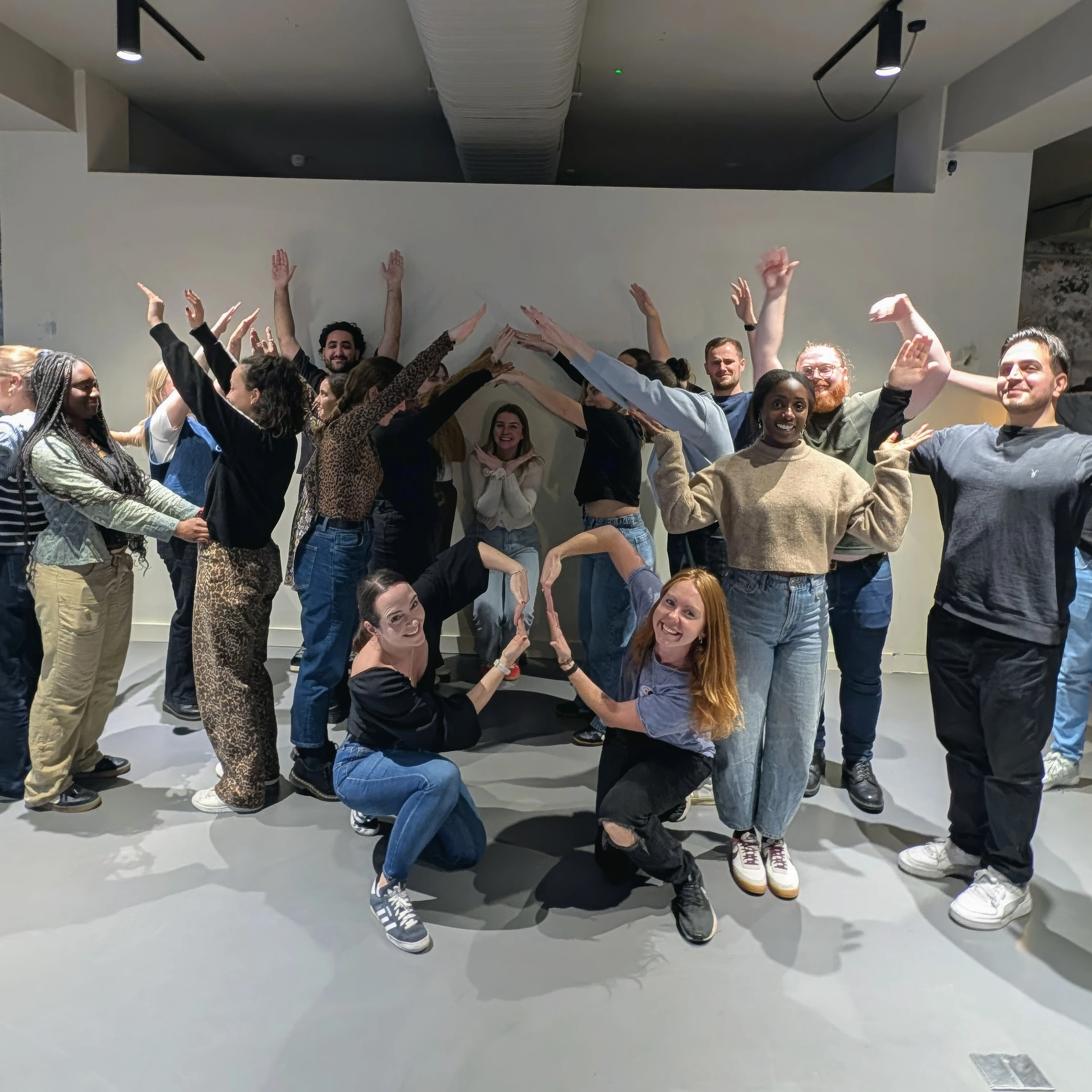 Medialab workplace group photo Photo of a group of people making shapes with their bodies in an office environment