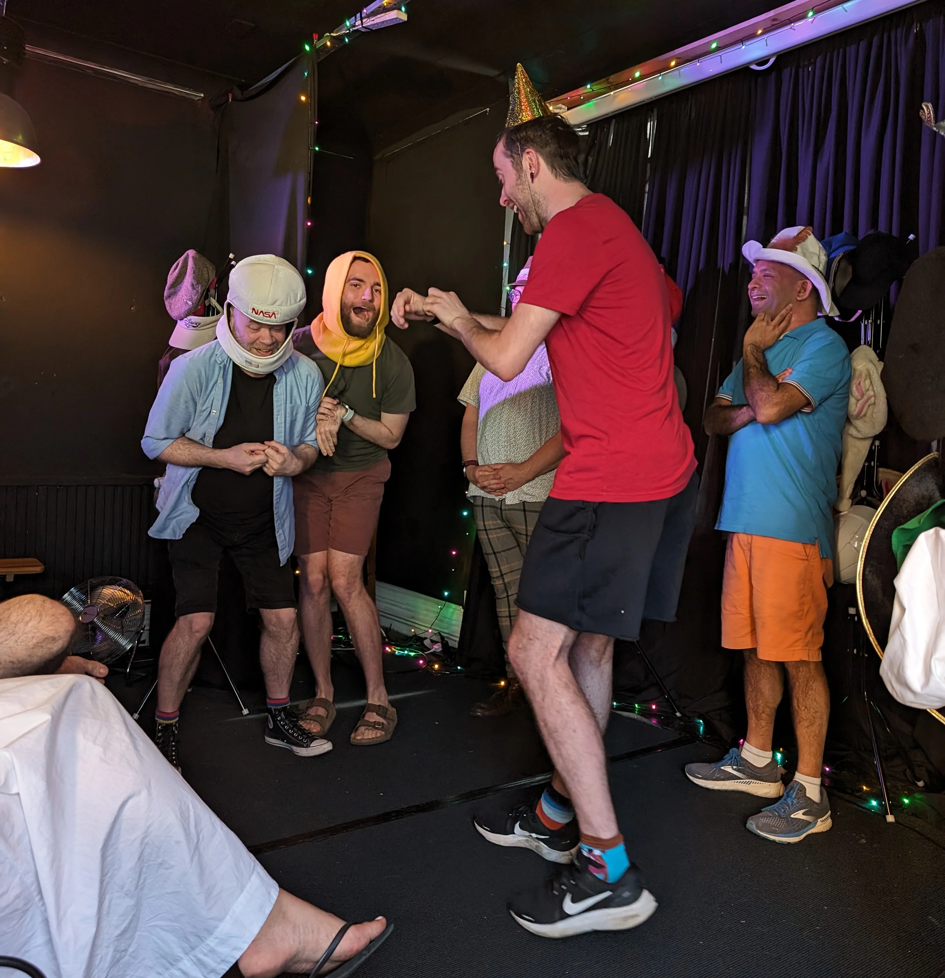 Improv team performing on stage in silly hats having a kangaroo fight