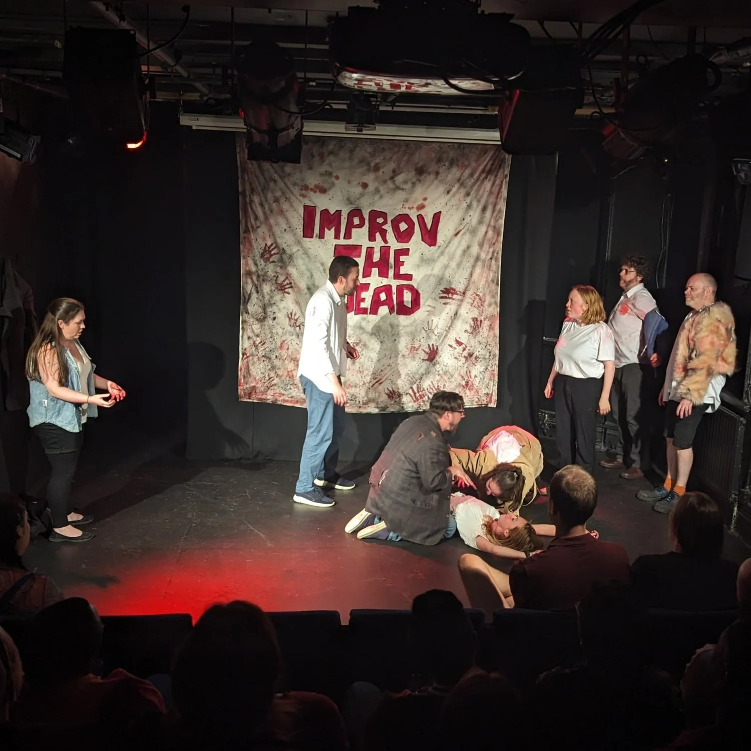 Improv the Dead doing a scene at Camden Fringe 2023 Improv comedy group Improv The Dead performing at the Camden Fringe 2023 in London. 8 performers on stage, some playing as zombies, the zombies are eating someone on the floor.