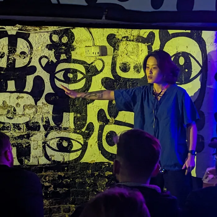Modern-art-eric Comedian on stage dressed in scrubs pointing to the left side