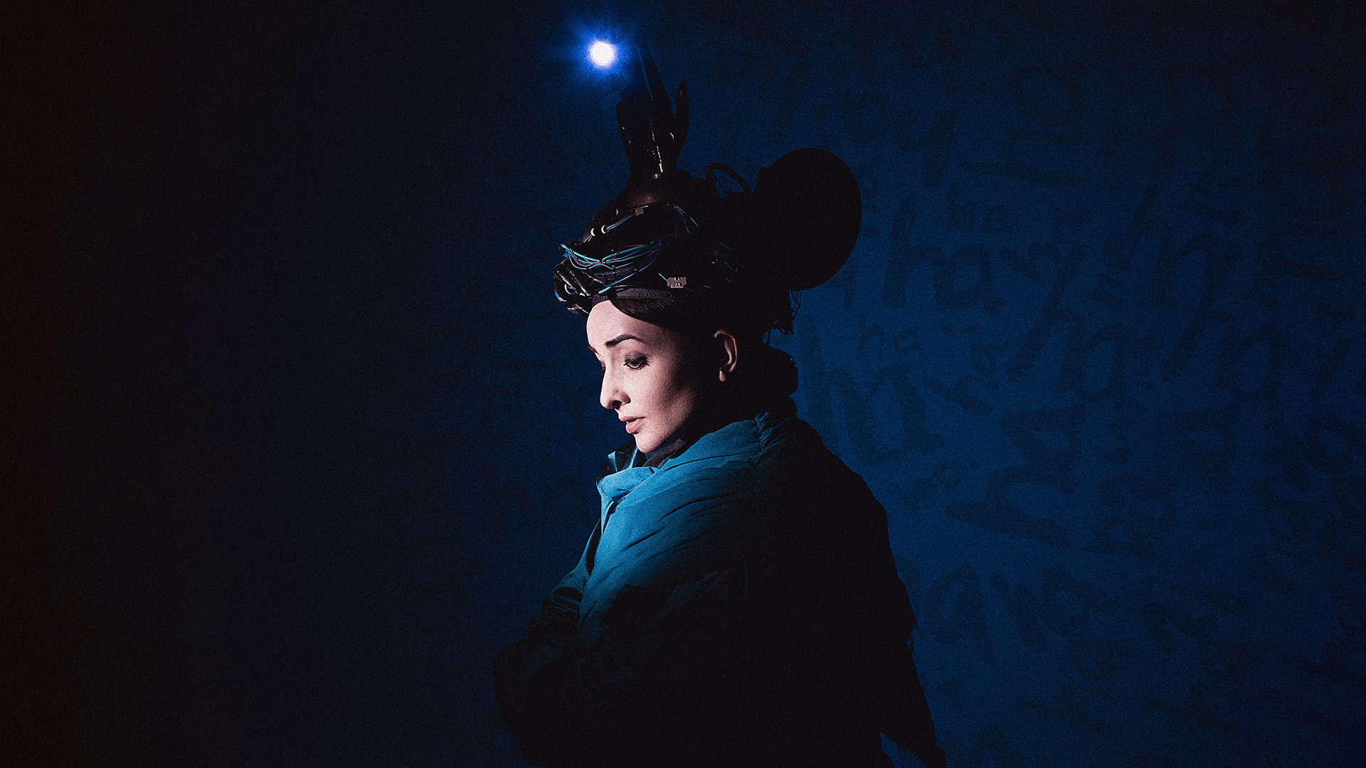 Dark image showing comedians Julia Masli in blue, only her face is illuminated and there is a small light bulb above her head