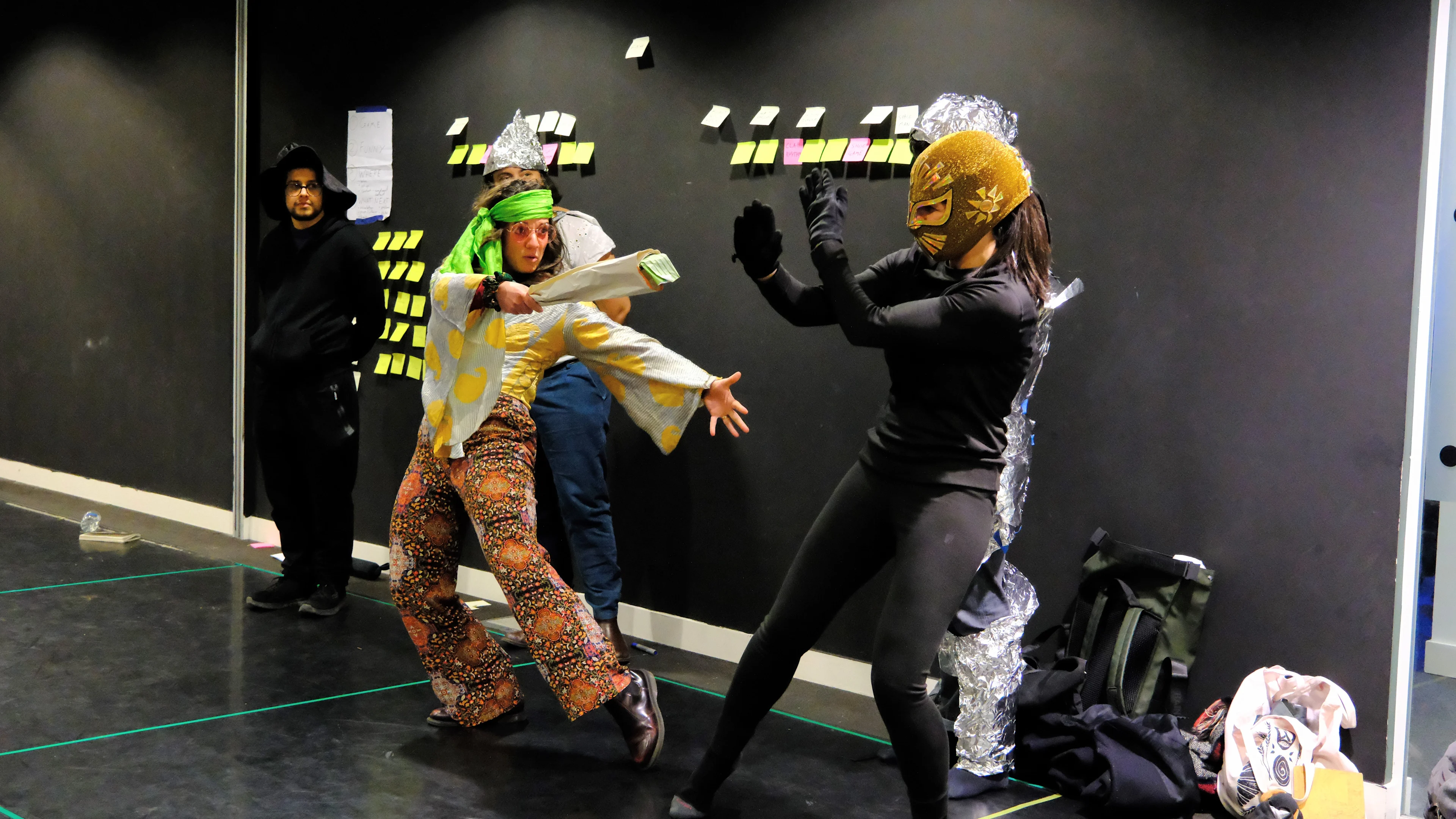 People in costumes stood against a back wall holding a newspaper in a fighting pose