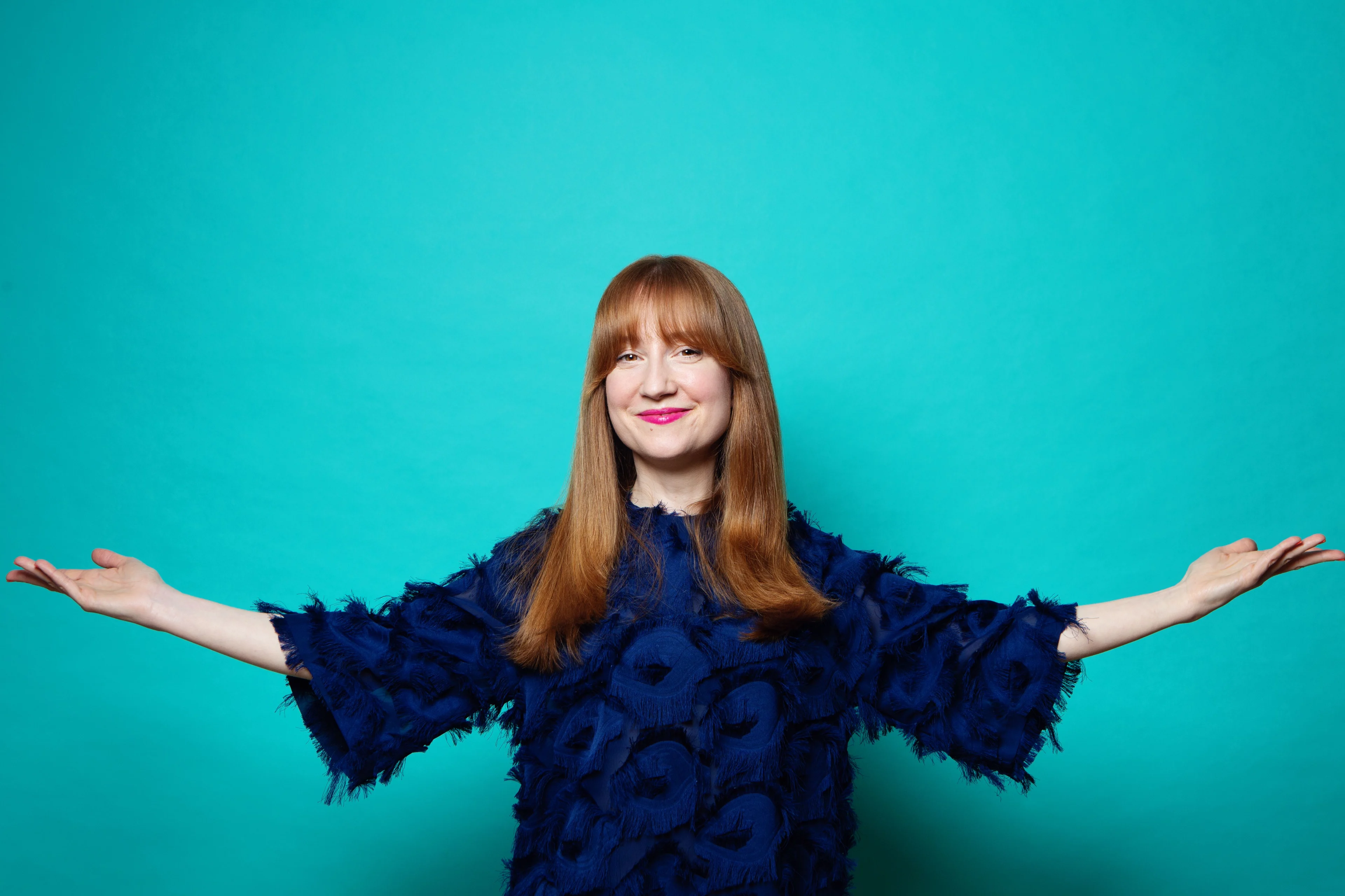 Susan with her arms wide, smiling and on a blue background