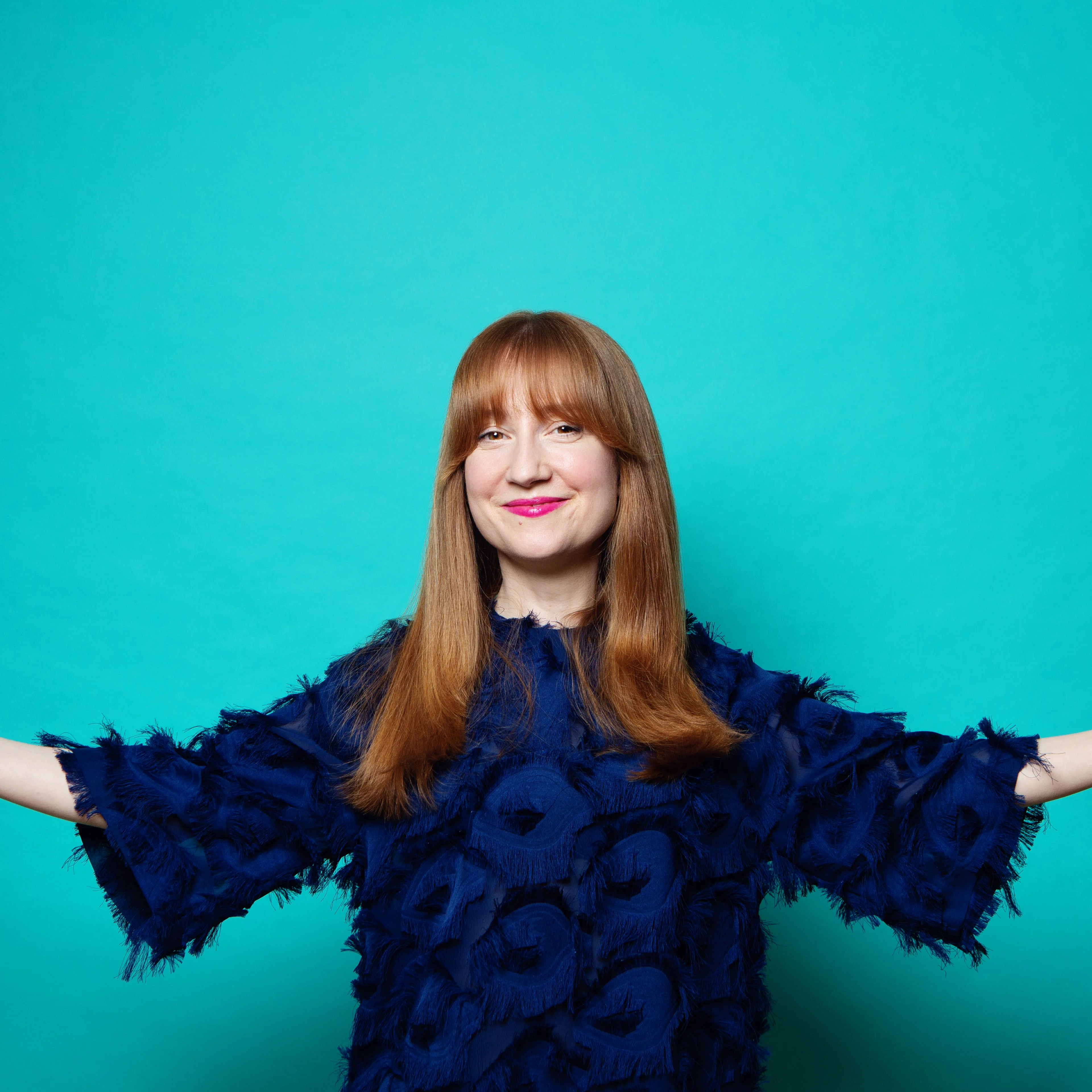 Susan Harrison Susan with her arms wide, smiling and on a blue background