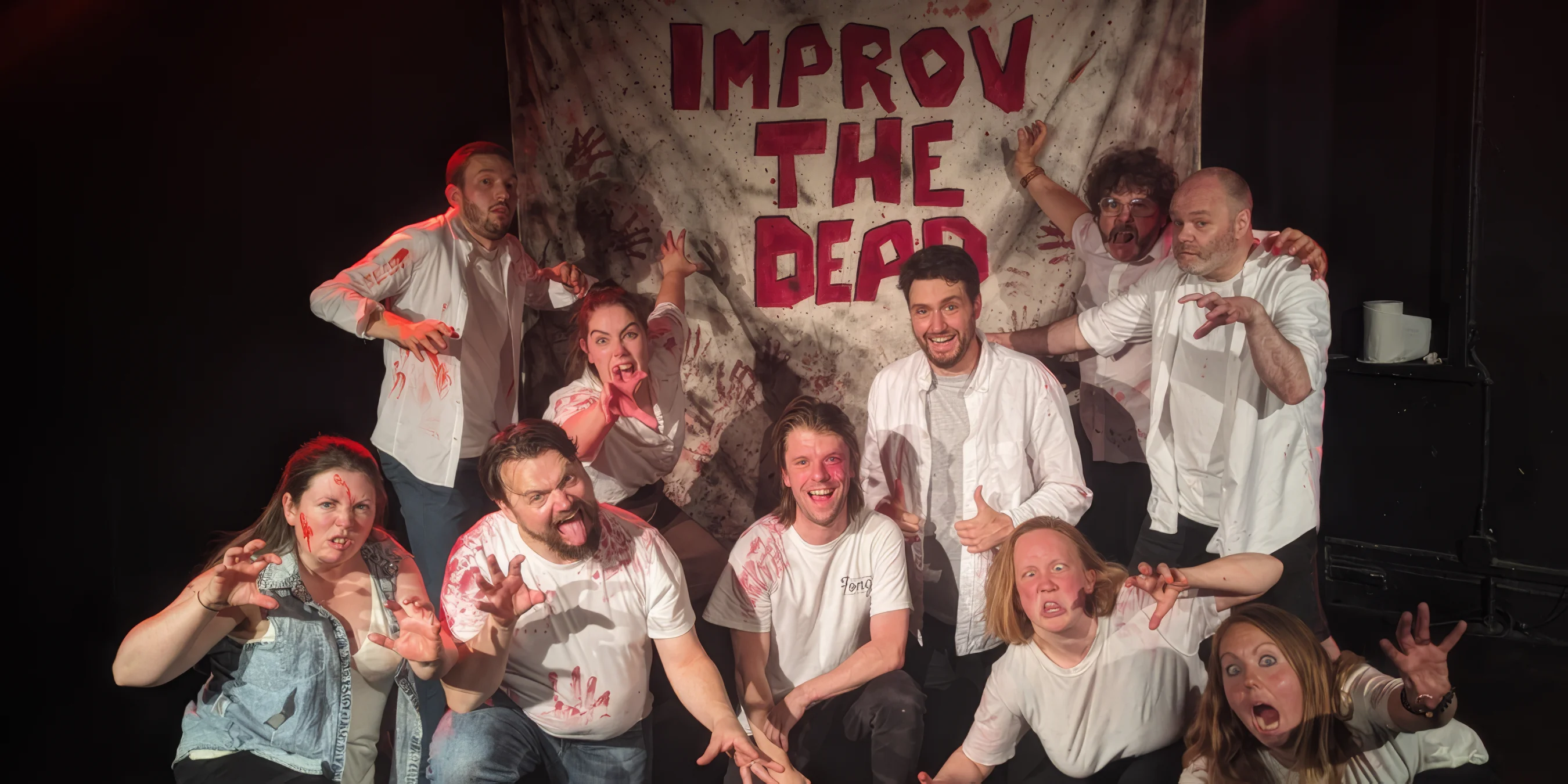 Improv team (10 people) posing like zombies in front of blood covered sign saying improv the dead 