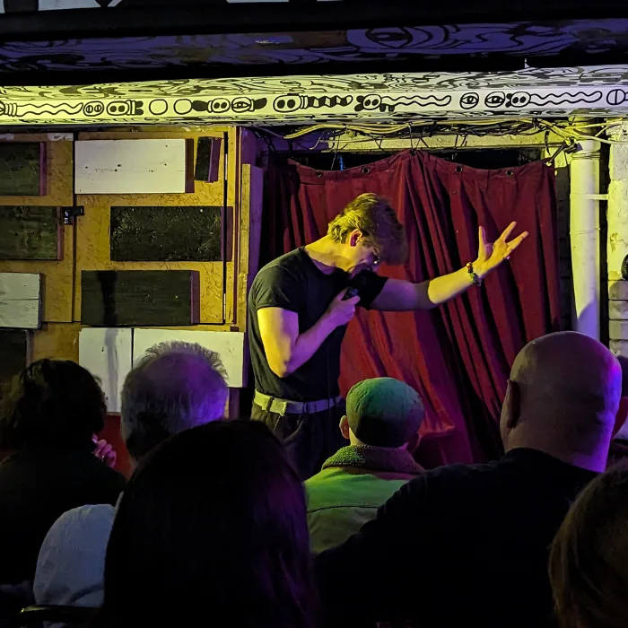Modern-art-Dru-cripps Comedian on stage holding a microphone and singing into it with his hand in the air in a powerful pose
