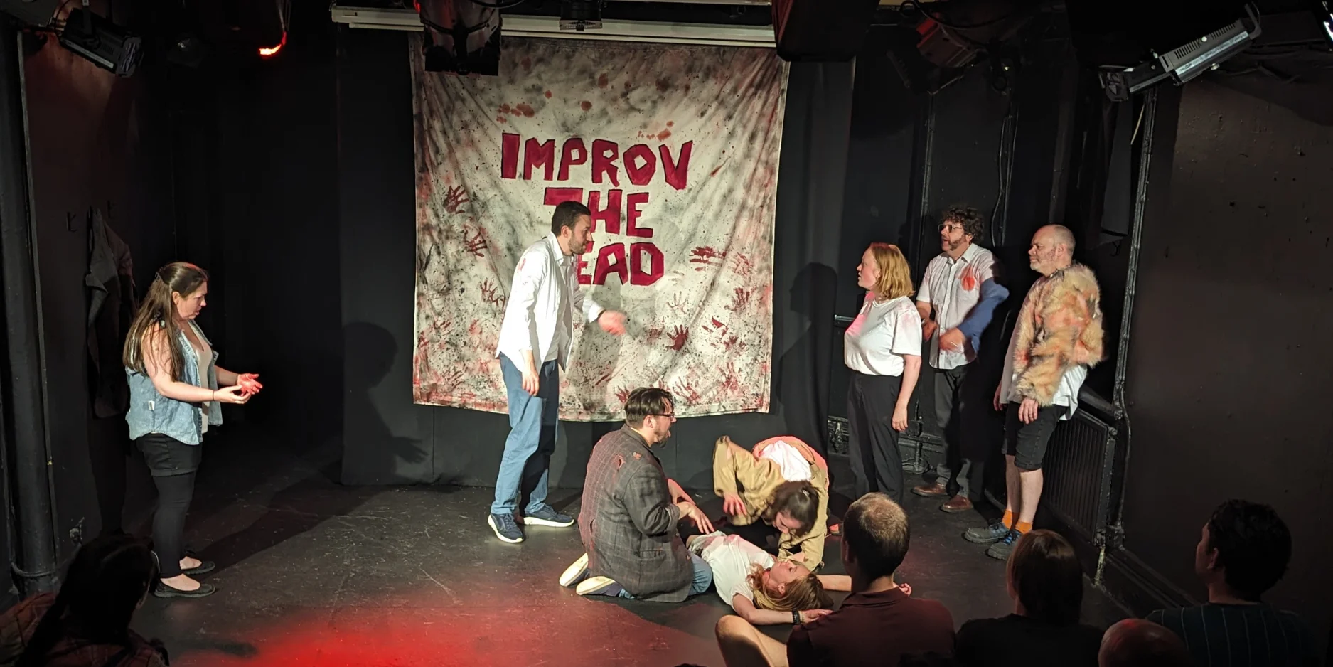 Improv the dead performing improv on stage. Actors are pretending to eat a corpse whilst covered in blood 