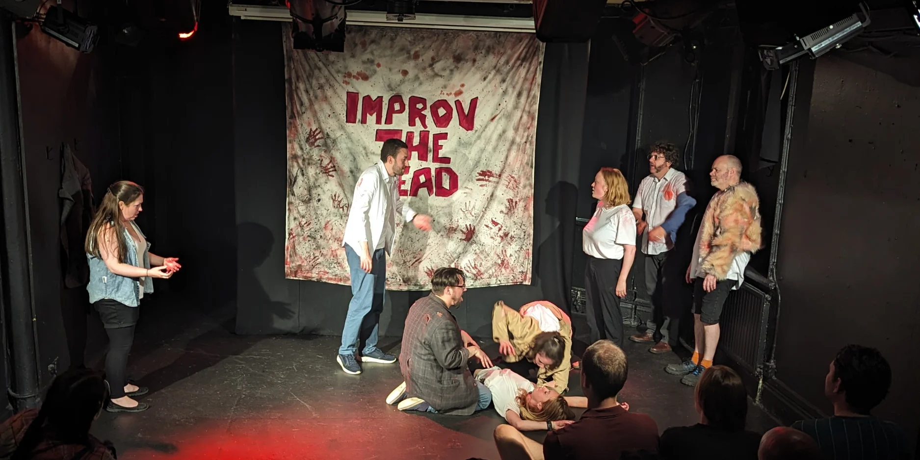 Improv the dead performing improv on stage. Actors are pretending to eat a corpse whilst covered in blood