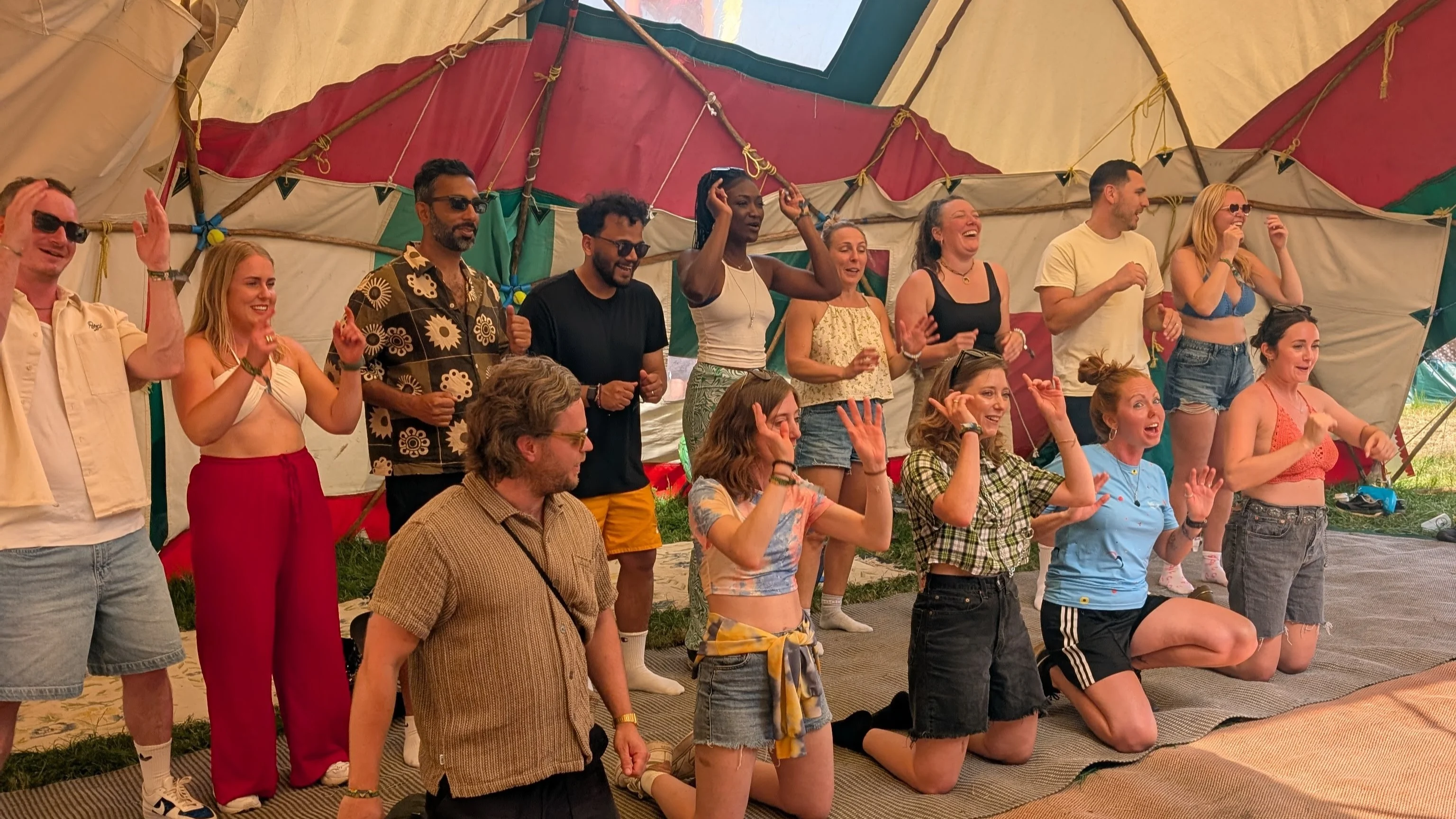 Group of people stood up or on their knees with their hands in the air singing inside a yurt