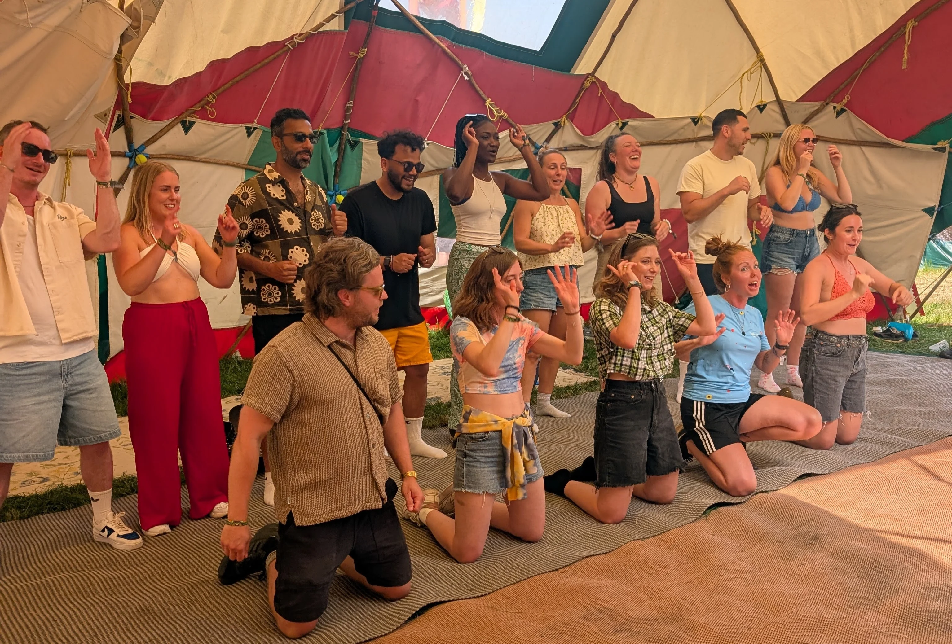 Group of people stood up or on their knees with their hands in the air singing inside a yurt