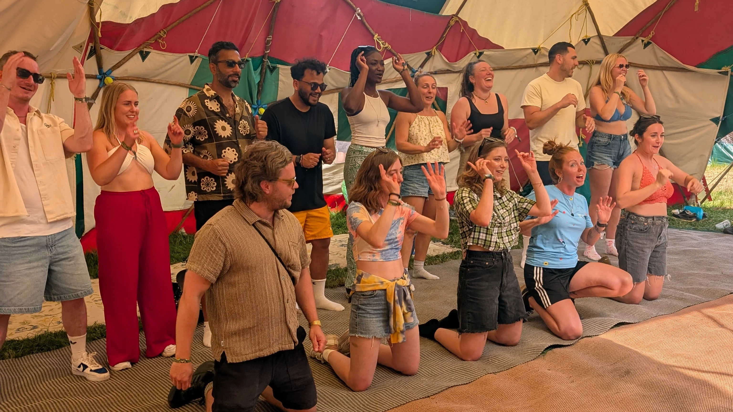 Glastonbury 2025 Group of people stood up or on their knees with their hands in the air singing inside a yurt