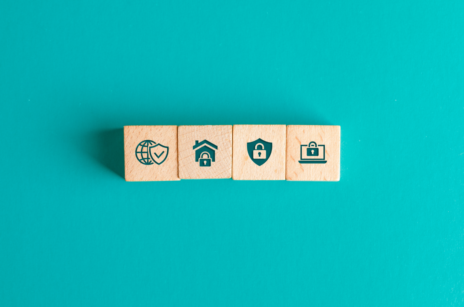 Vier Symbole zum Thema Webseiten und Datenschutz auf Holzklötzen liegen auf türkisfarbenem Tisch.