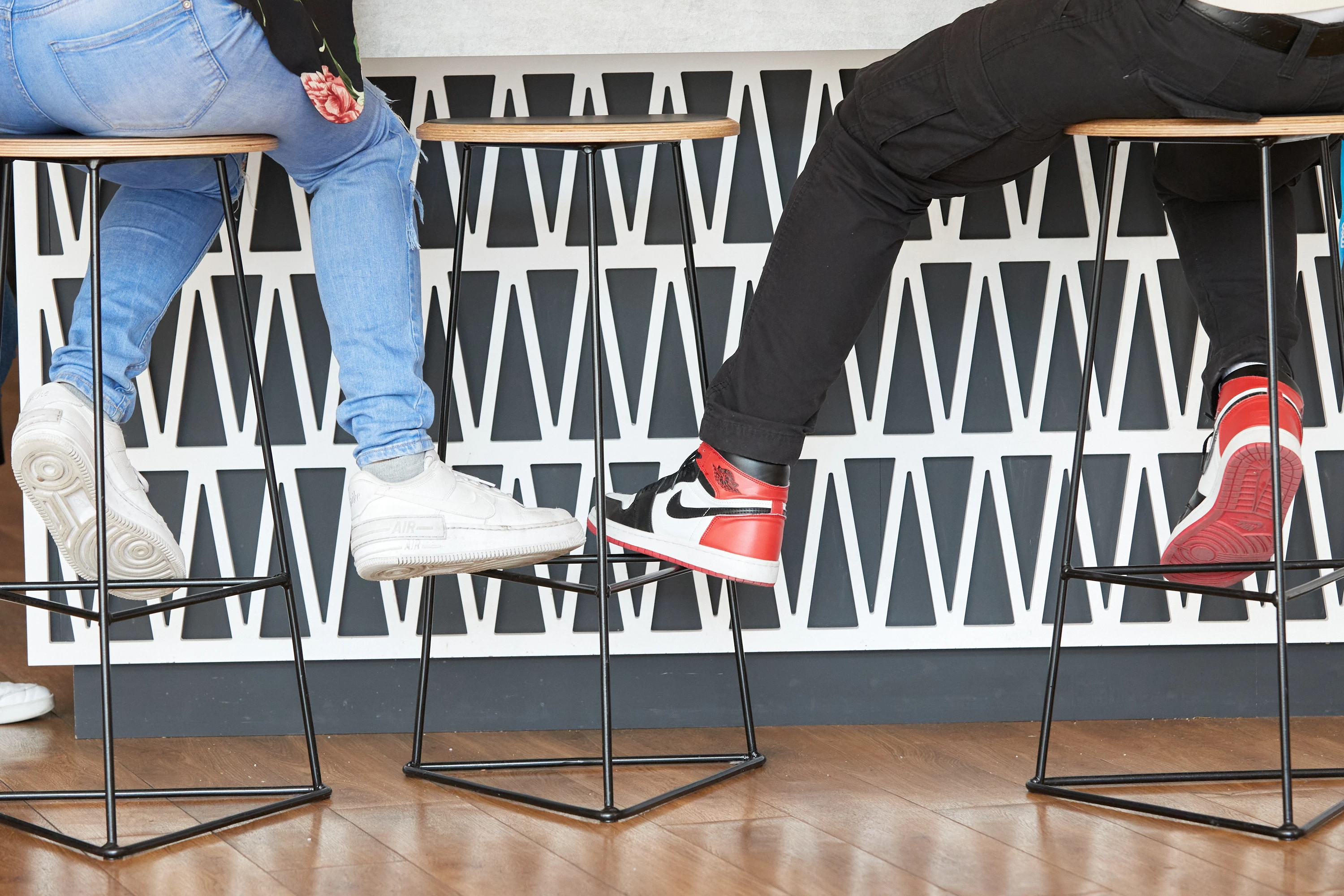 A photo of two people sitting on the high bar type chairs, wearing colourful sneakers.