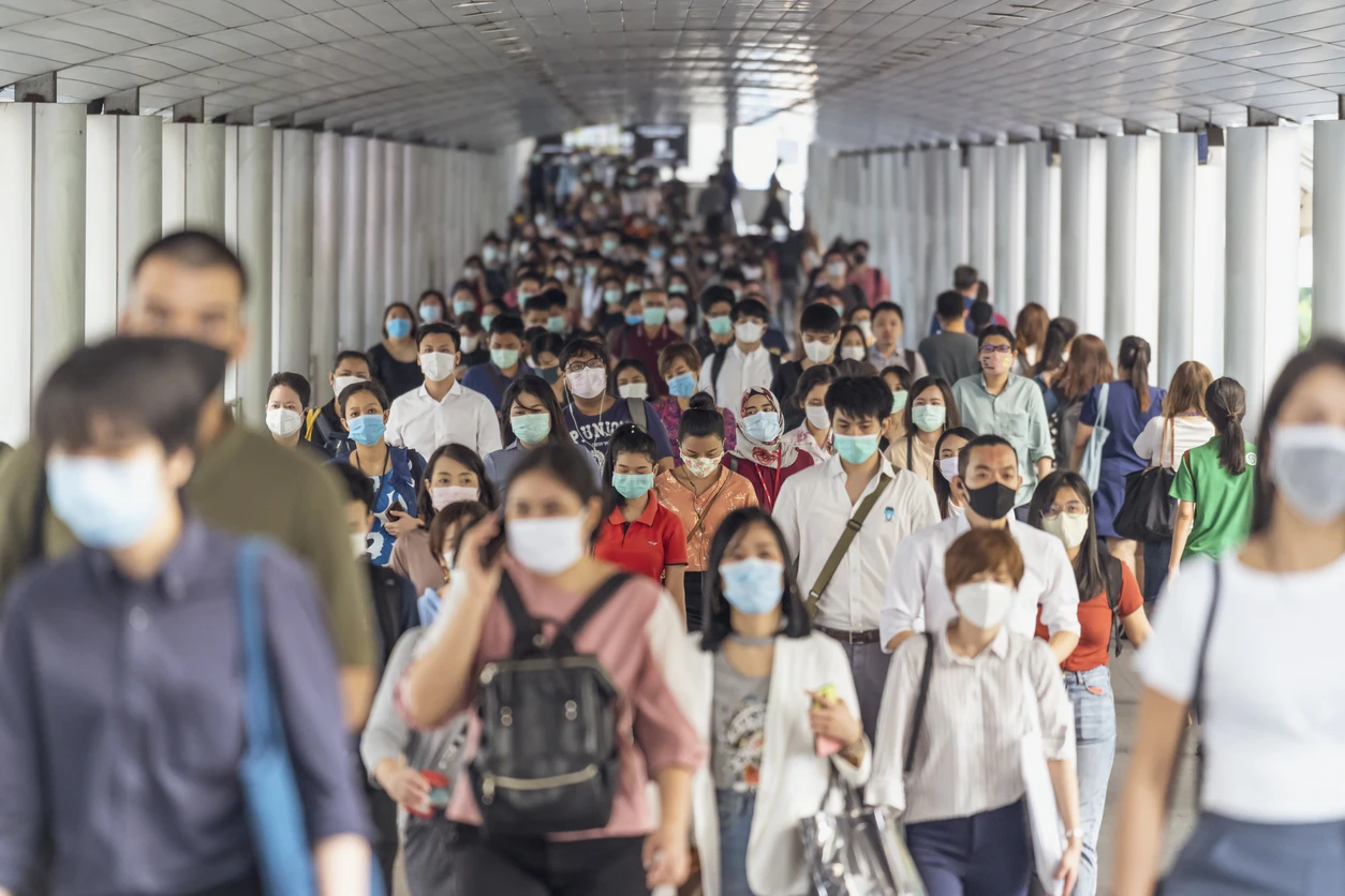 A crowd walking through a tube station space, wearing masks.