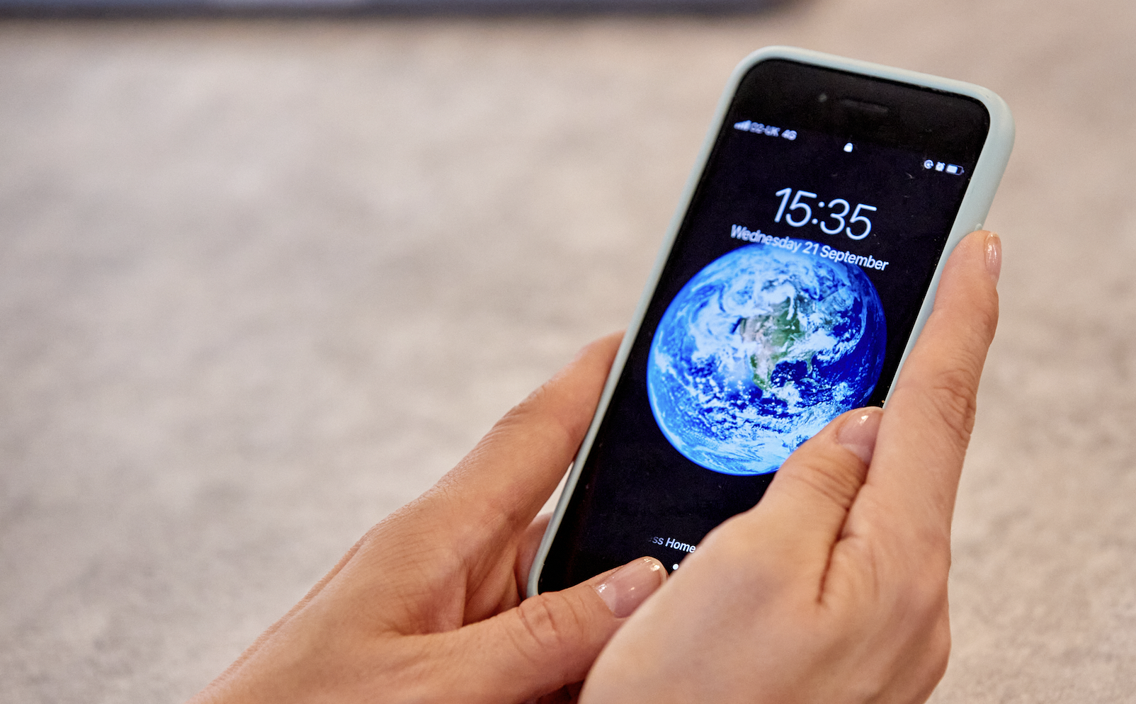 A photo of woman's hands holding a smartphone. The screen of the smartphone displays a photo of Earth seen from space.