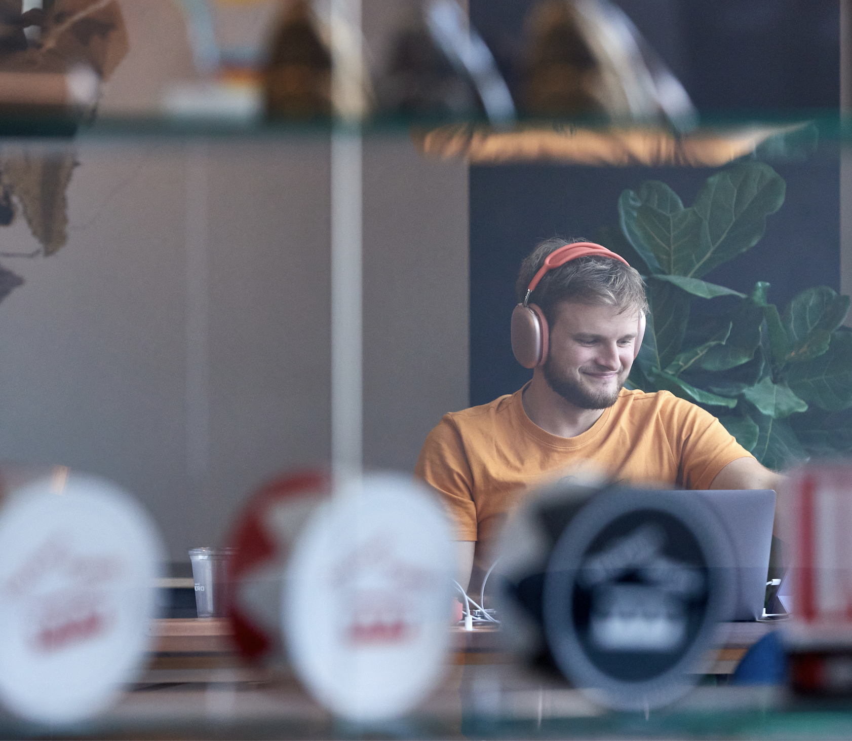 A photo of a man wearing bright yellow headphones, smiling, working on his lap top. An out-of-focus digital design awards are on the shelf in front of him.