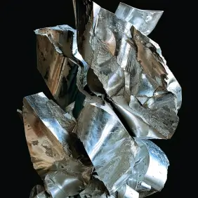 Twisted, jagged piece of zinc. The metal is shiny, with a reflective surface that catches the light, creating a mix of silver and blueish hues. The object appears to be crumpled or folded in a complex, irregular shape, with sharp edges and creases. The dark background contrasts with the bright, polished metal.